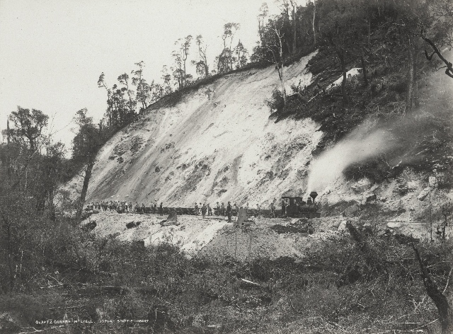 An historical image of the train track cut into the side of a bare hill. The locomotive can be seen to the left of the picture.