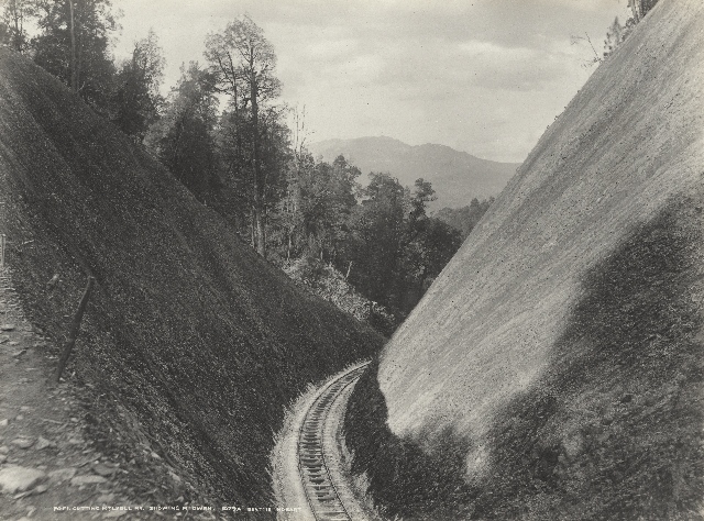 A historical image of the railway line snaking its way in between two steep, bare hills.