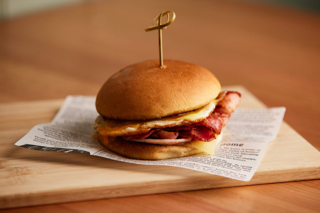 An egg and bacon roll sits on a wooden board.