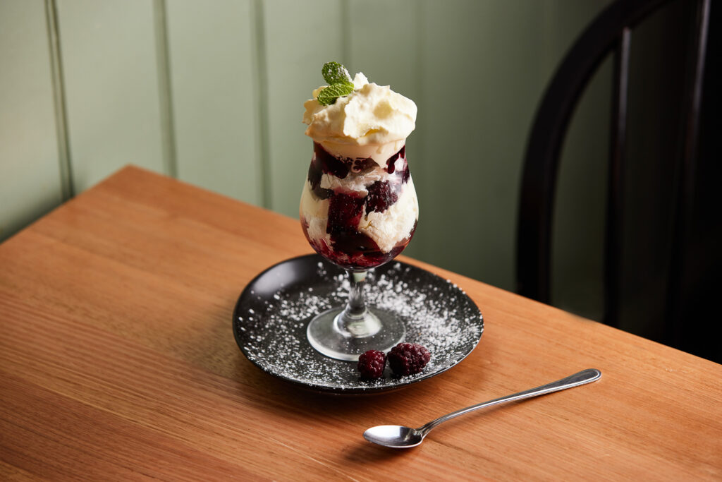A decadent looking dessert sits in a cocktail glass. It is topped with cream and a sprig of mint.