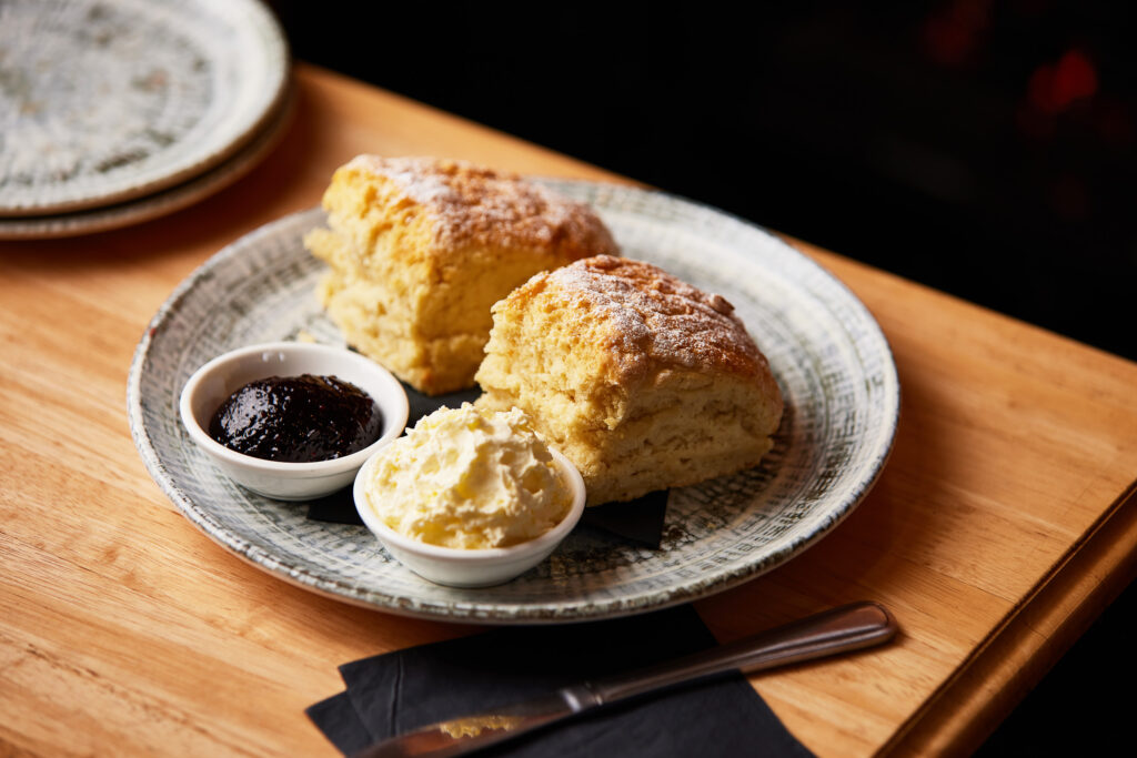 A plate of two enormous scones sits next to ramekins with cream and jam.