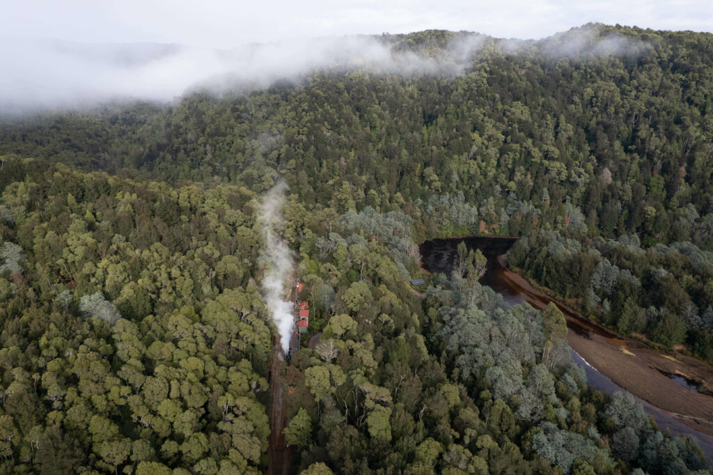 An overhead image of Lower Landing Station with a train sitting alongside the platform. The station is surrounded by rainforest and the King River sits off to the right.