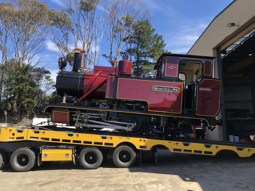 Abt Locomotive No. 2 sits on top of a large yellow truck, being offloaded carefully at Carswell Park.