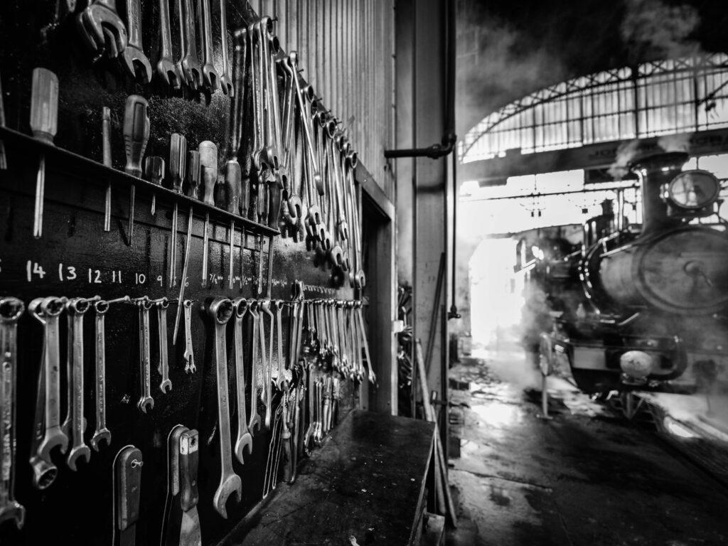 A wall of clean tools inside the loco shed is neatly outlined on the board behind. The inside of the shed is steamy.
