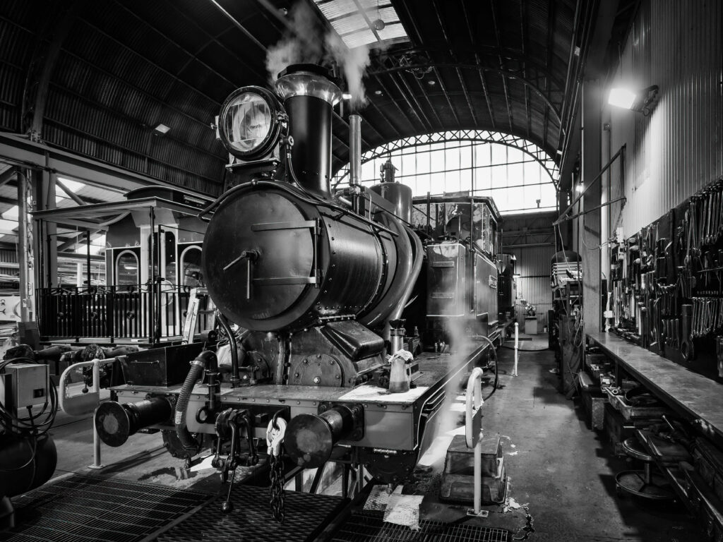 An original Abt steam locomotive sits inside the logo shed with the arched glass and steel windows behind it.