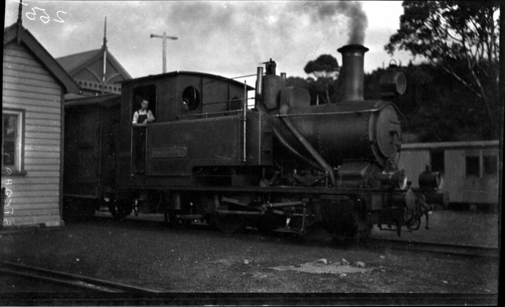 Historical image of Abt loco no. 4 with a man standing inside the cabin. The image looks to have been taken at Regatta Point Station in Strahan.